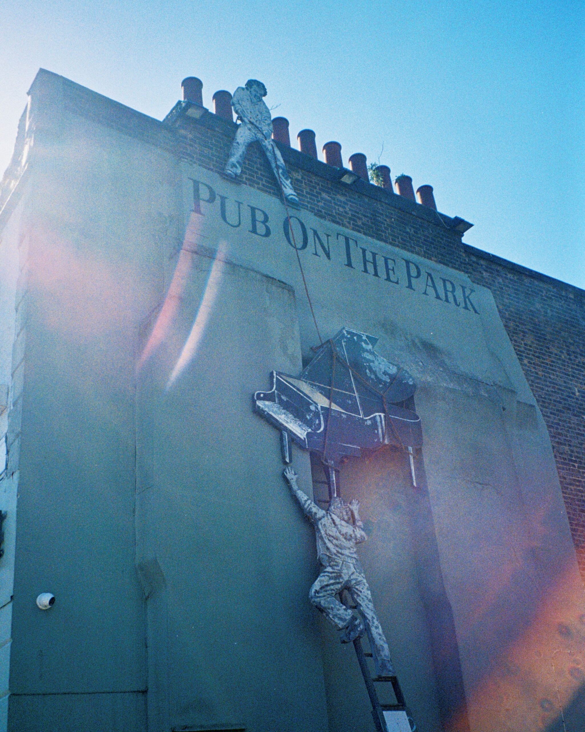 Photo of the 3d decal on the side of the pub that shows two people trying to pull a grand piano up a ladder to the roof.
