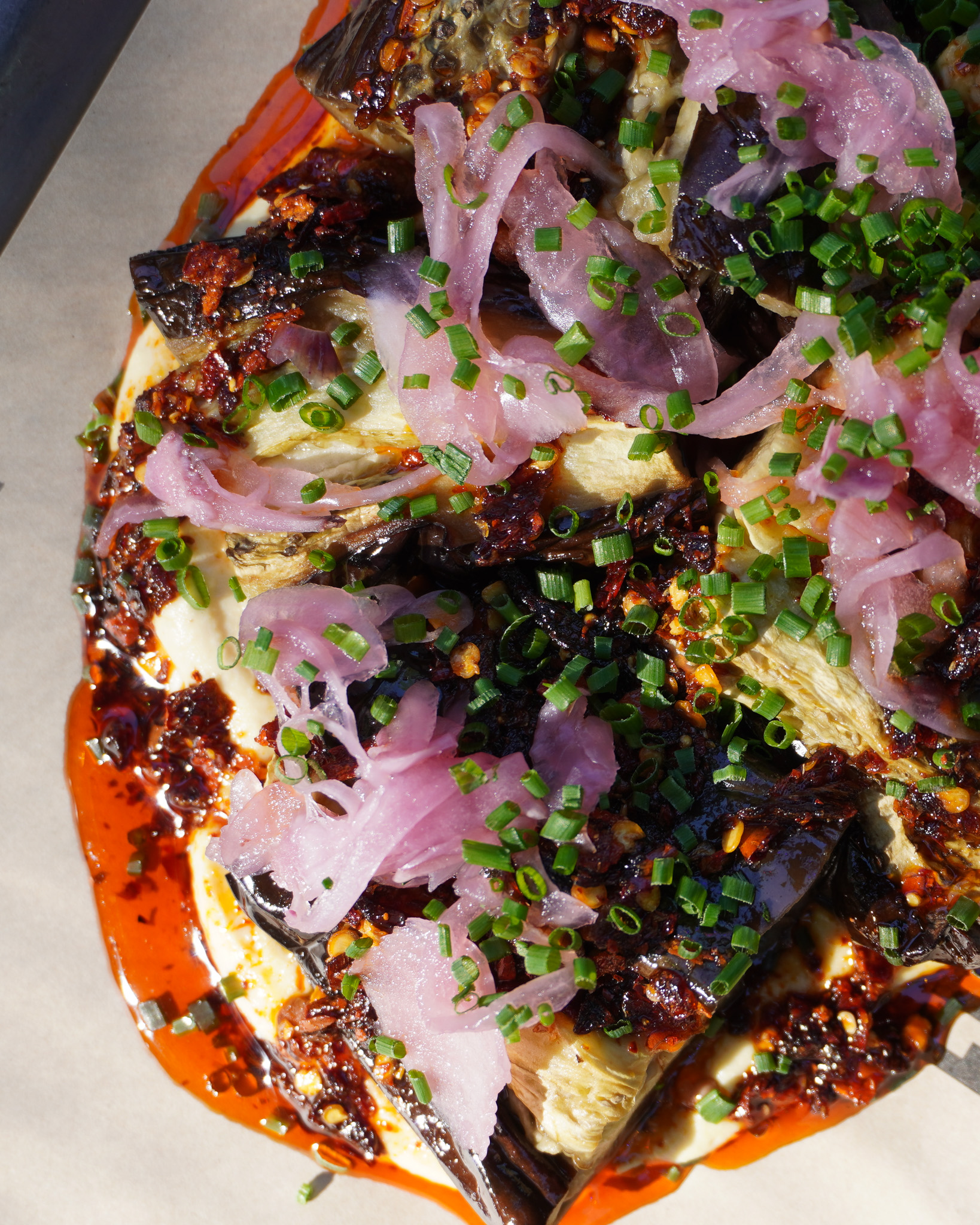 Vegan and Gluten Free Roasted Aubergine topped with pickled red onions, crispy chilli oil and on a bed of whipped lemon hummus