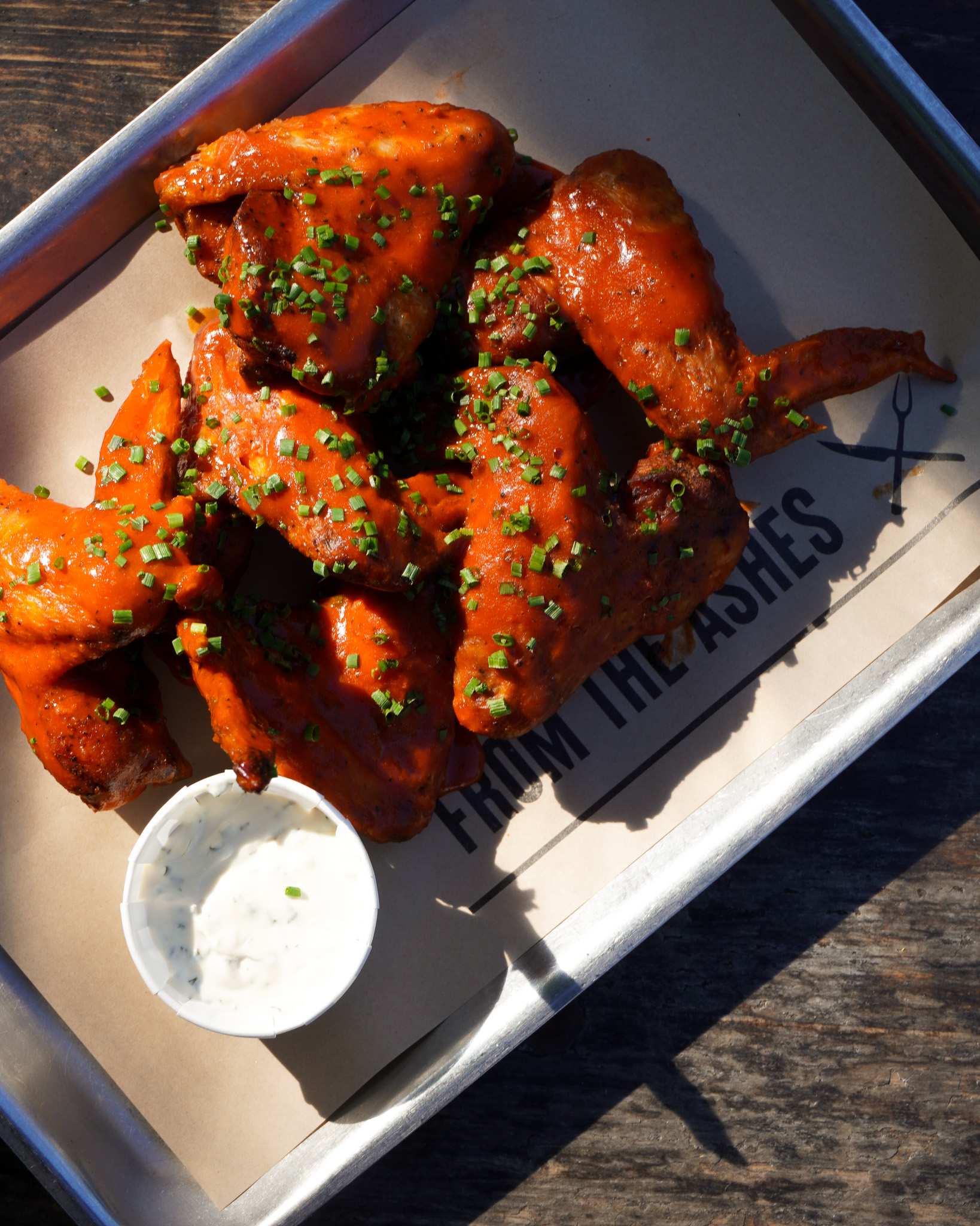 A tray of chicken wings covered in buffalo sauce with a pot of ranch dip
